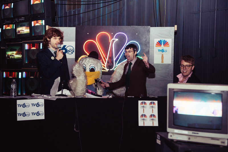 The party was broadcast live on YouTube by comedians in the Special Features improv troupe, who re-created a cringe-y four hour broadcast of the fair’s opening day. Josh Shreve annotated like a reporter breaking down amid chaos as Scott Anderson held a microphone up to the party’s mascot, “Seymore D. Icks,” a mockery of the fair’s fluffy pelican avatar Seymore D. Fair. Nearby, Sam Moody took a break from anchor duty to laugh at the feed on a live monitor. Photo: Akasha Rabut.